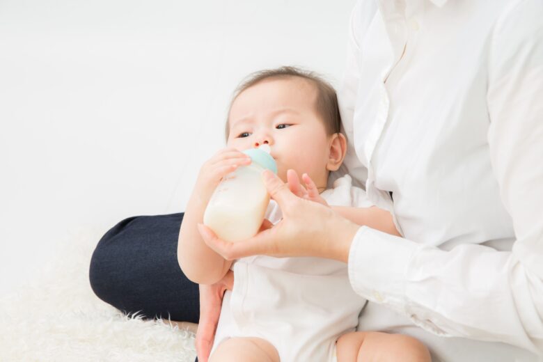 大人に抱えられた赤ちゃんが哺乳瓶でミルクを飲んでいる様子
