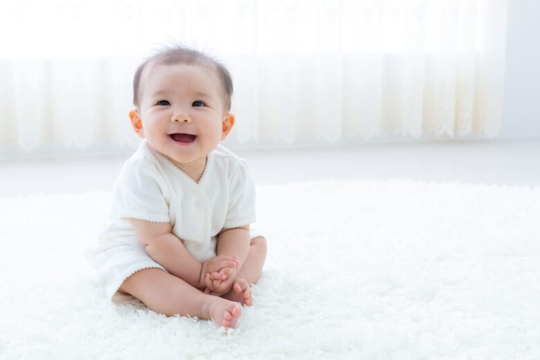白いカーペットの上で笑顔で座る赤ちゃん